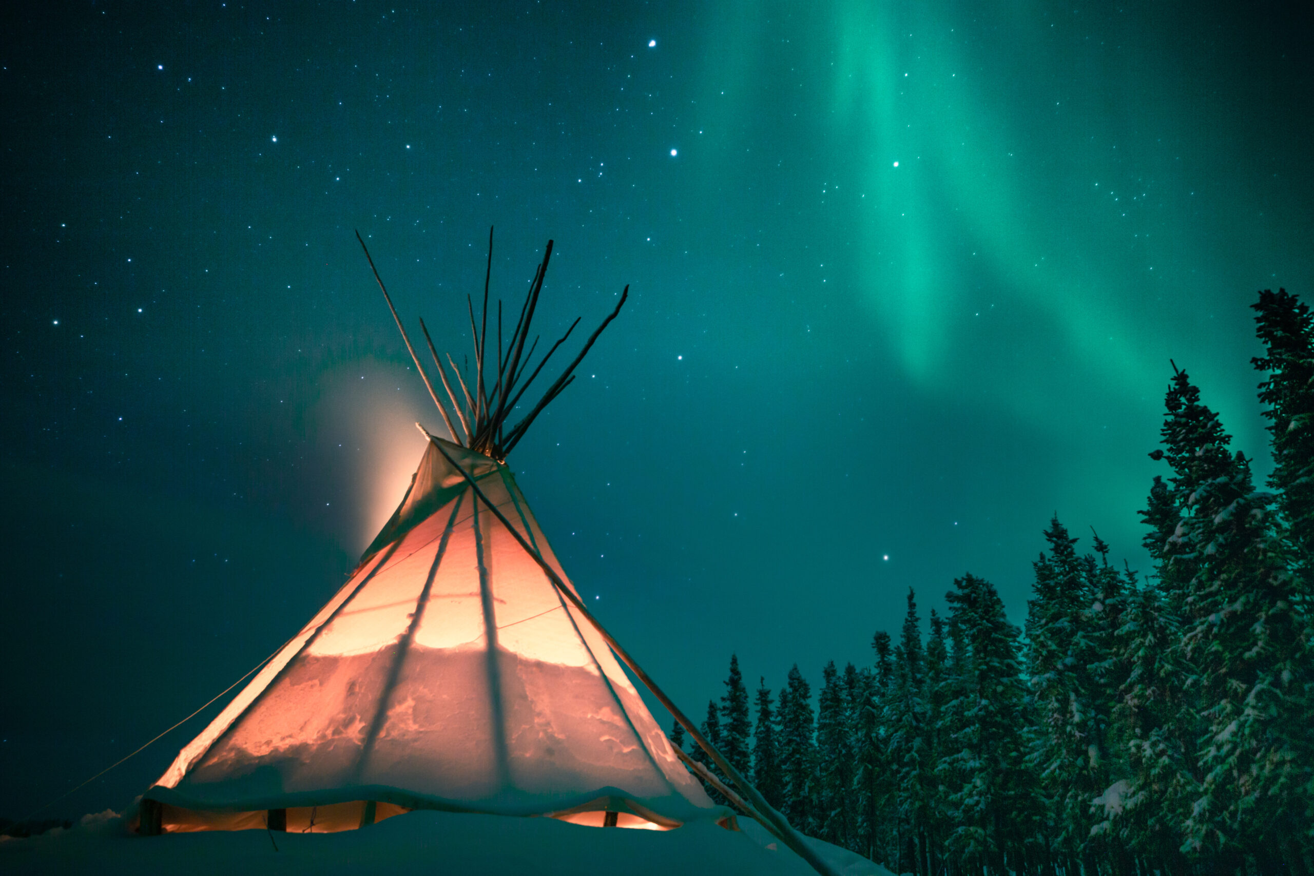 Glowing tipi / teepee in the snowy forest under the northern lig